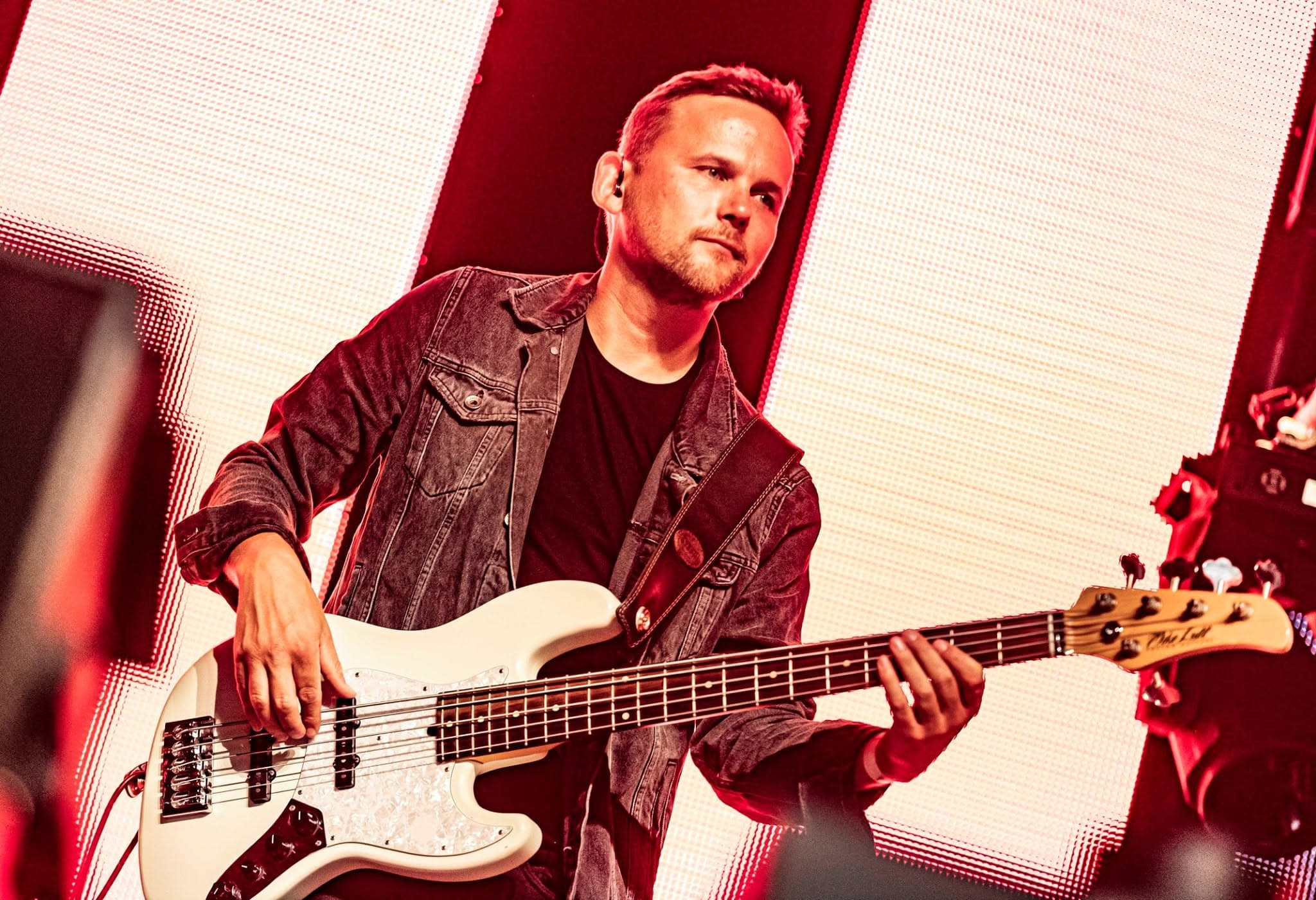 Bert van Uffelen speelt basgitaar op het podium, in rood licht